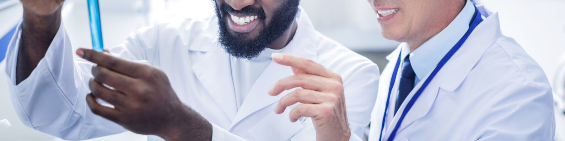 Pleasant positive scientist standing behind his colleague Professional scientists. Pleasant nice positive scientist standing behind his colleague and smiling while looking at the test tube
